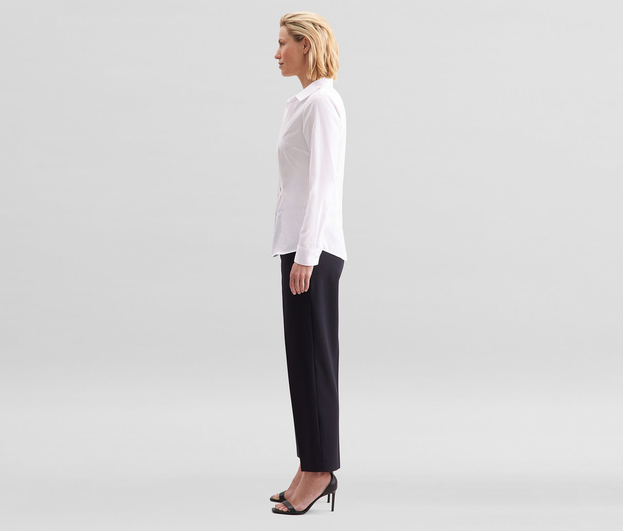 Femme de profil, portant un chemisier Slim Fit non iron Seidensticker blanc et un pantalon noir.