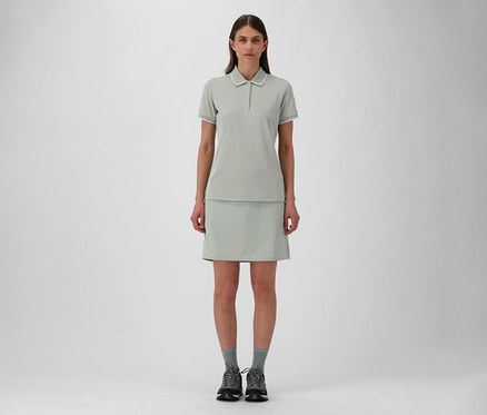 Femme portant une jupe d’extérieur CMP et un polo pour femme CMP en piqué stretch pistache, avec des chaussettes grises et des chaussures de randonnée.