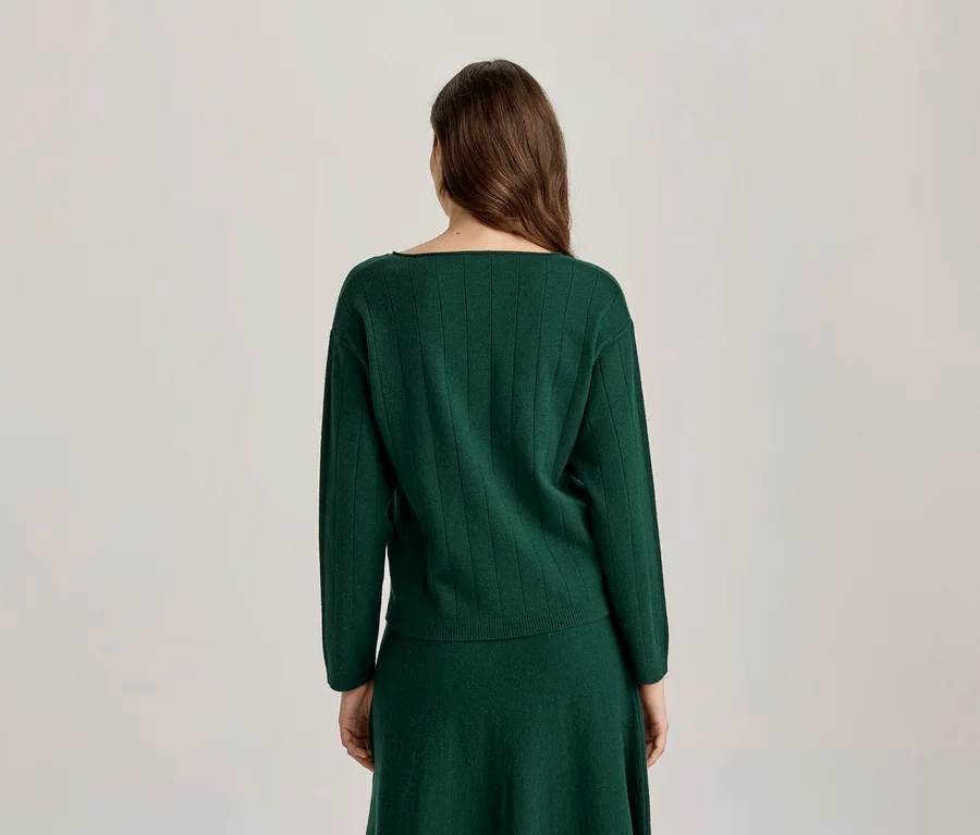 Femme vue de dos portant un pull côtelé vert foncé et une jupe assortie.