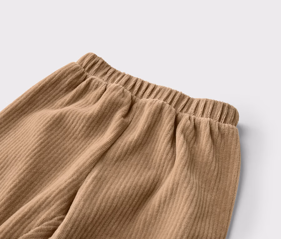 Gros plan d'un pantalon en velours côtelé beige avec une taille élastique, montrant la texture côtelée du tissu.