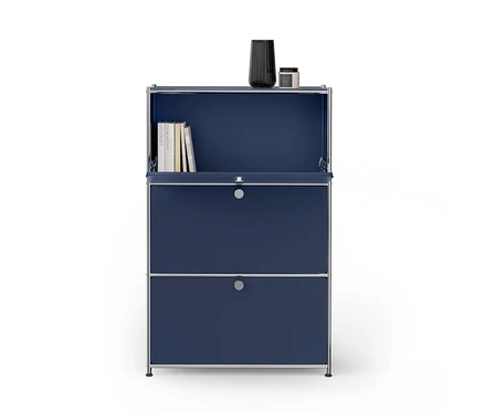 Meuble modulaire bleu foncé avec cadre chromé. La section supérieure est ouverte, montrant des livres à l'intérieur. Un vase noir nervuré et une petite bougie sont posés dessus. Deux sections fermées avec des poignées argentées sont en dessous.