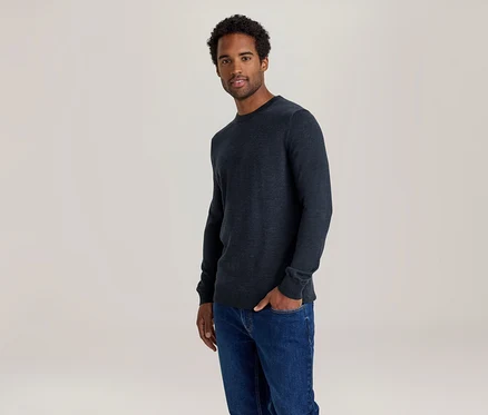 Homme en pull bleu foncé et jean, une main dans la poche.