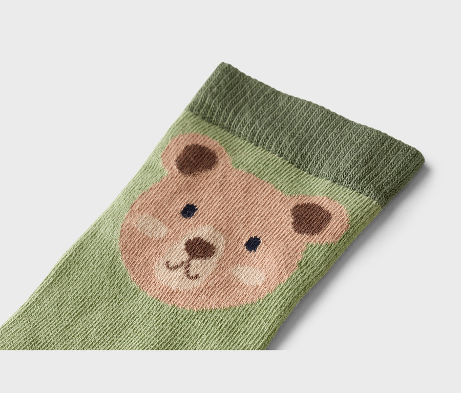 Gros plan d'une chaussette vert clair avec un visage d'ours dans les tons marron et rose.