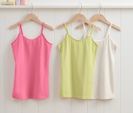 Trois maillots de corps enfant (3 pièces) suspendus à des cintres en bois : rose, vert et blanc.