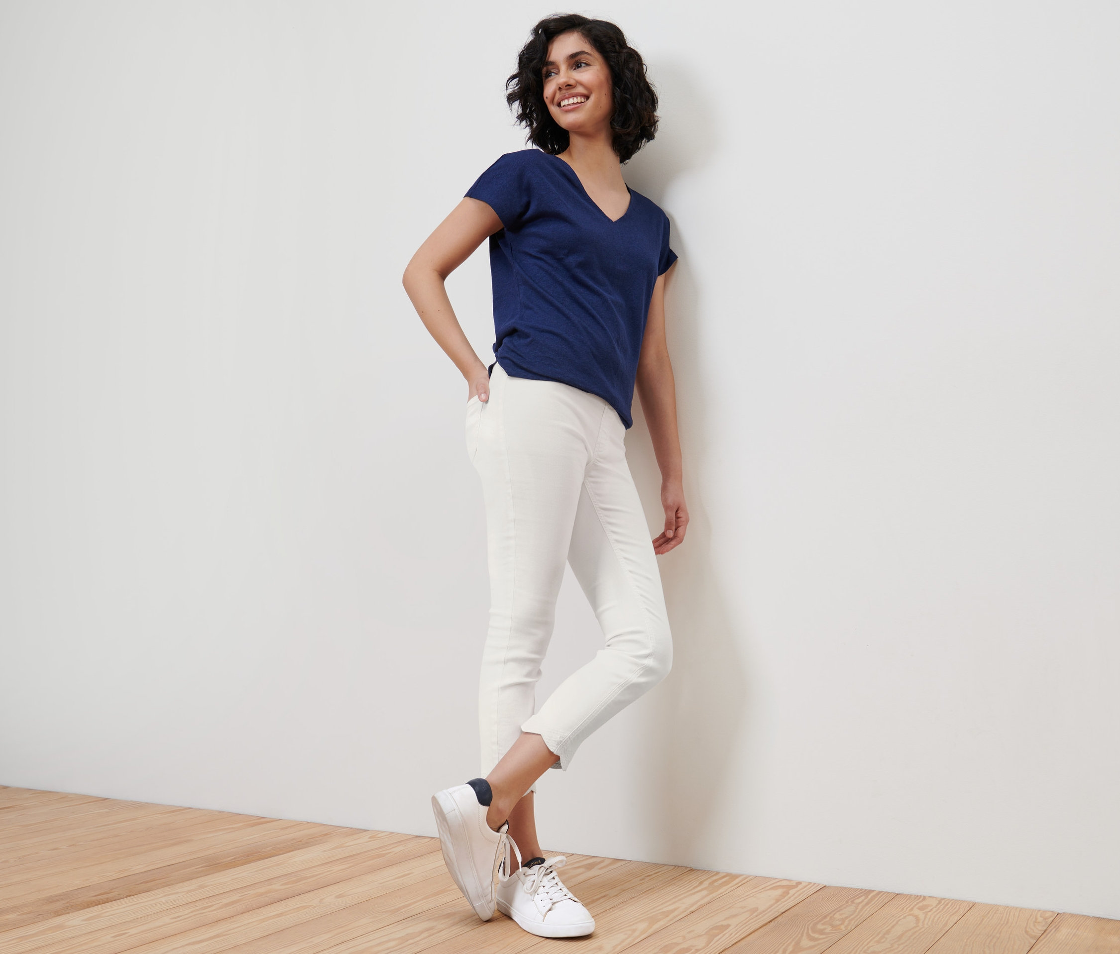 Une femme souriante appuie contre un mur et porte un t-shirt bleu et un tregging 7/8 à broderie ajourée blanc.