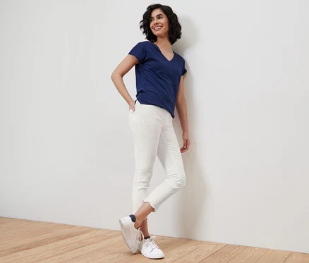 Une femme souriante appuie contre un mur et porte un t-shirt bleu et un tregging 7/8 à broderie ajourée blanc.