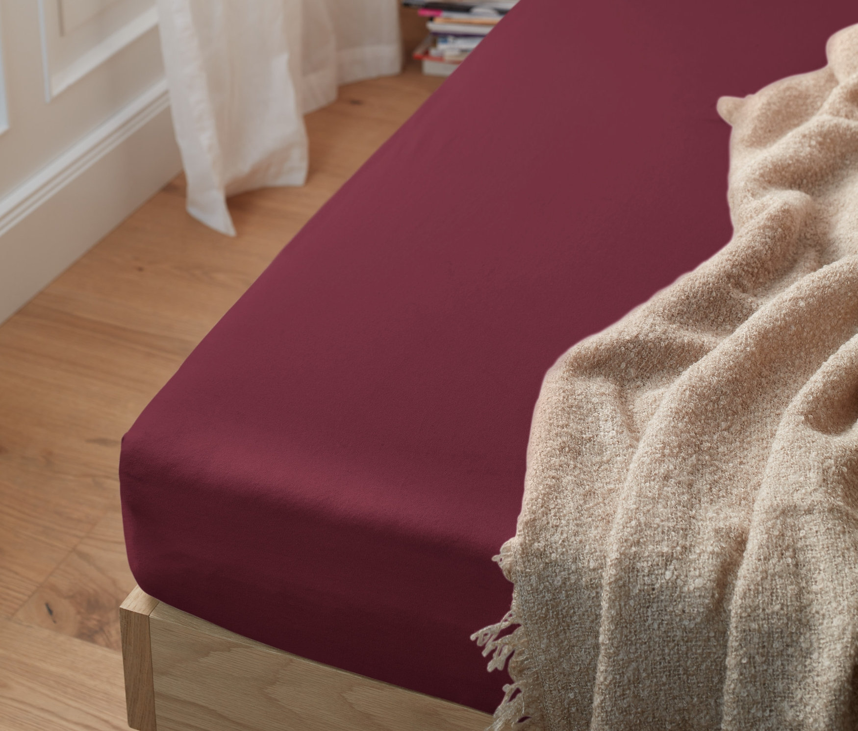 Vue détaillée d'un lit en bois avec un drap-housse en jersey rouge foncé.