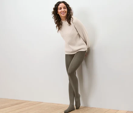 Une femme appuyée contre un mur portant un collant thermique et un pull.