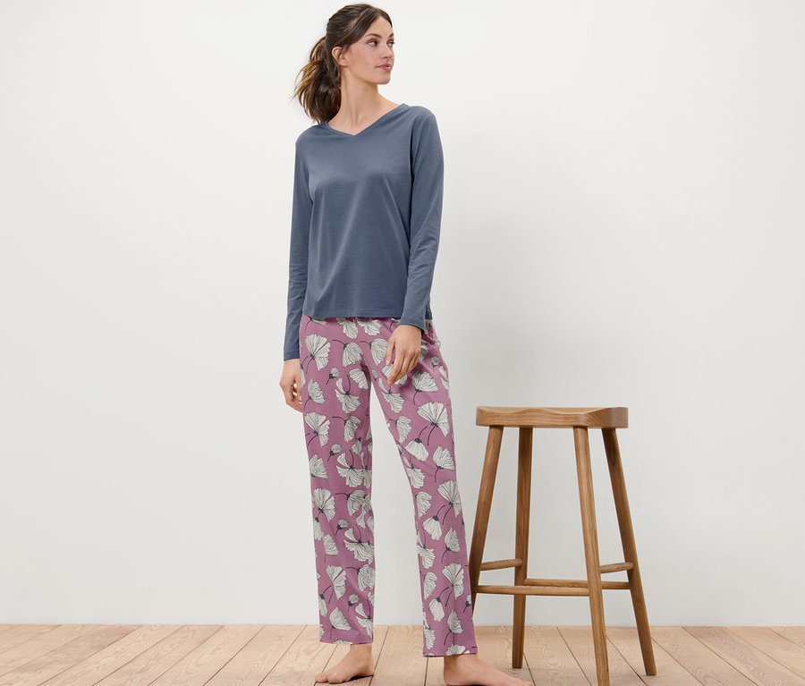 Une femme se tient à côté d'un tabouret en bois et porte un pyjama à fleurs.