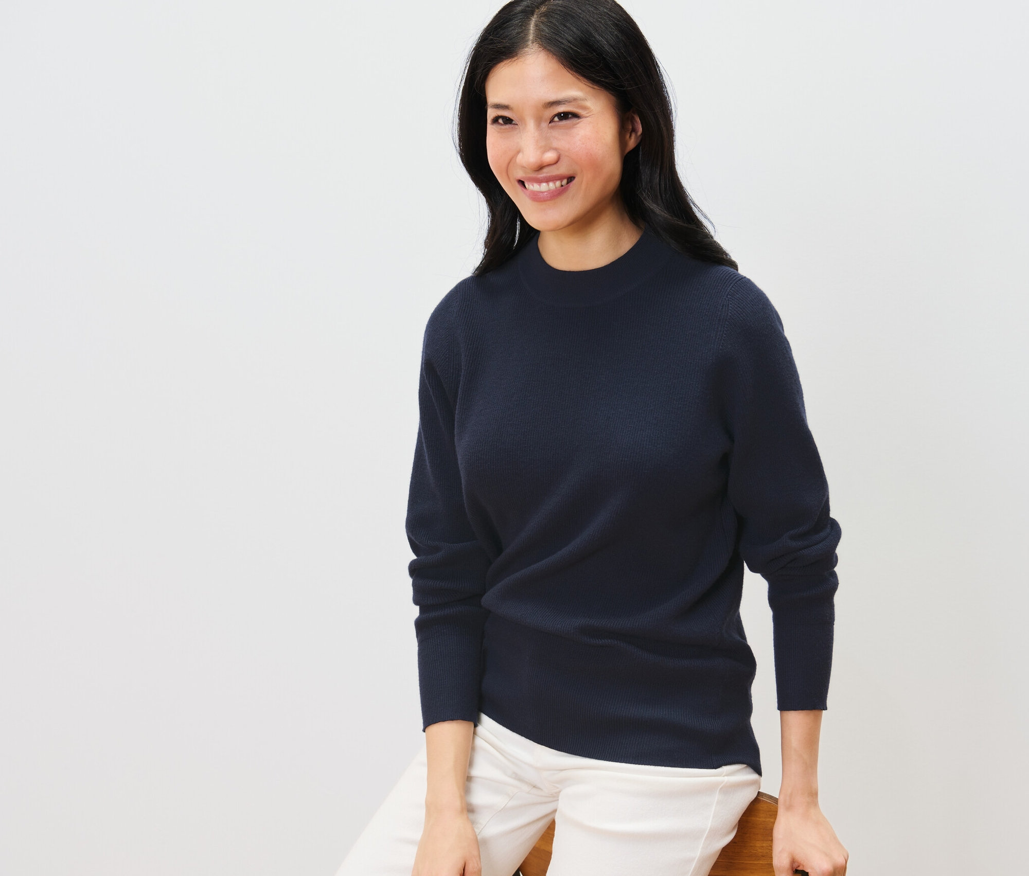 Une femme est assise et porte un pull en maille fine bleu foncé.