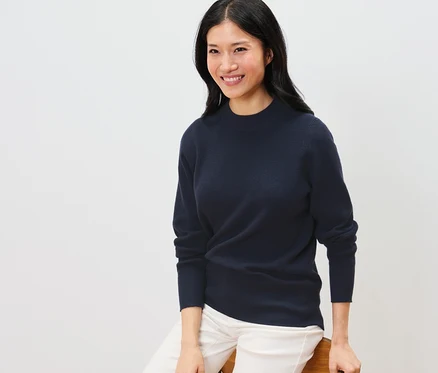 Une femme est assise et porte un pull en maille fine bleu foncé.
