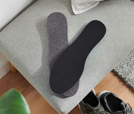 Deux semelles intérieures thermiques reposent sur un banc gris à côté d'une paire de chaussures grises.