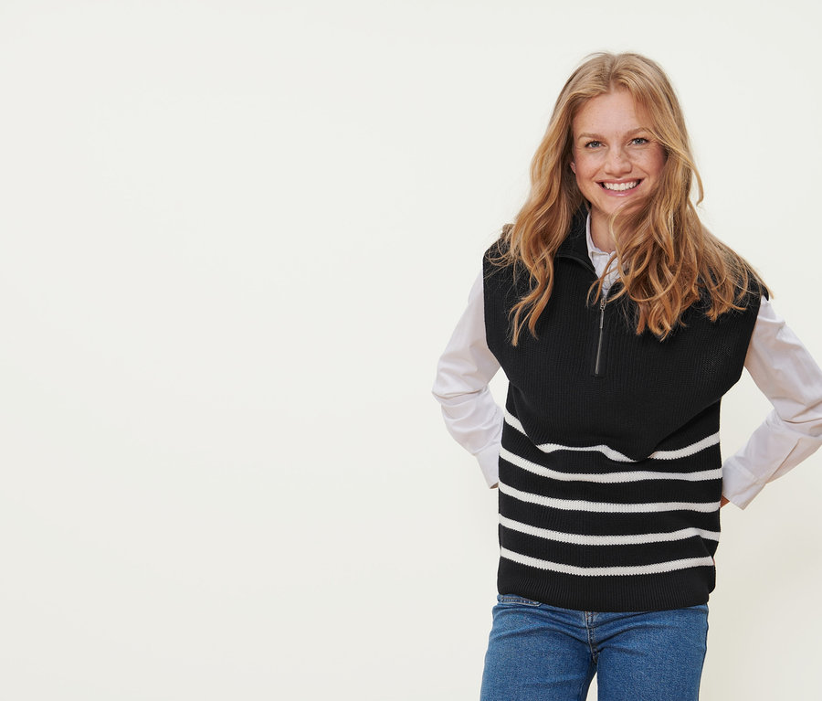 Une femme souriante portant un sous-pull à col camionneur noir rayé.