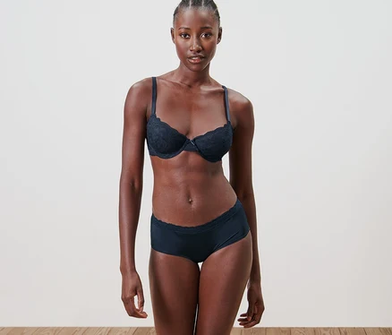 Femme noire posant en sous-vêtements. Elle porte un soutien-gorge et 5 culottes.