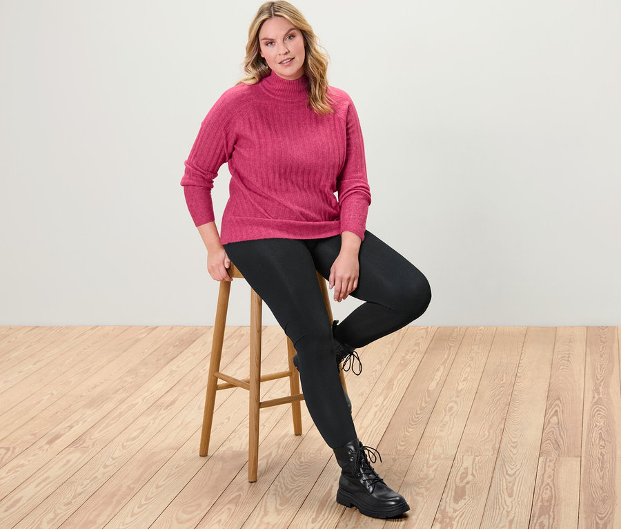 Une femme est assise sur un tabouret et porte un pull en maille côtelée à col montant et un legging thermique.