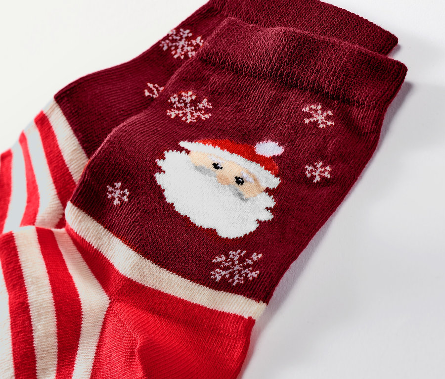 Gros plan d'une paire de chaussettes de Noël bordeaux avec des motifs de Père Noël et de flocons de neige.