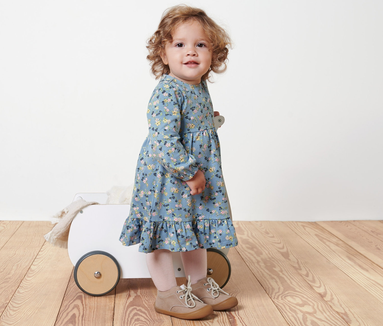 Une petite fille se tient à côté d'un chariot blanc et porte une robe en jersey pour bébé.