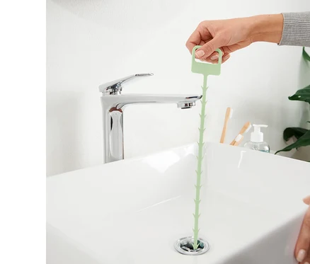 Une main insère 2 tiges de curage pour canalisations dans le drain d'un lavabo.