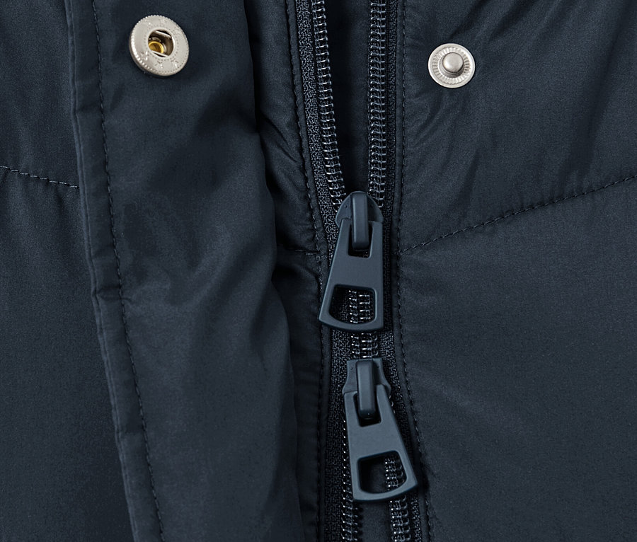 Gros plan sur un manteau matelassé à capuche bleu foncé montrant la fermeture éclair et les boutons-pression.