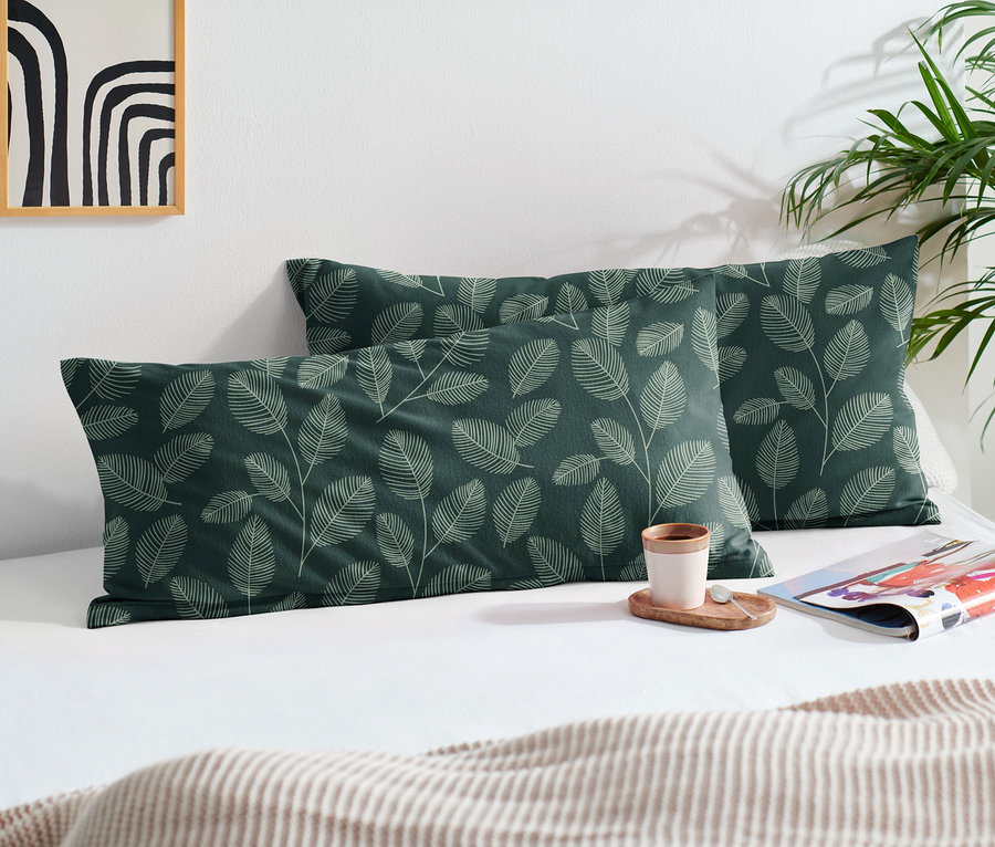 Deux taies d’oreiller en molleton vertes avec un motif de feuilles sur un lit.