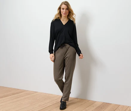 Une femme blonde pose, portant un haut noir et un pantalon de jogging avec jacquard pied-de-poule.
