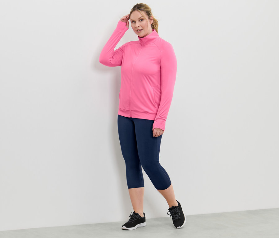 Femme portant une veste technique rose vif et un legging bleu marine.
