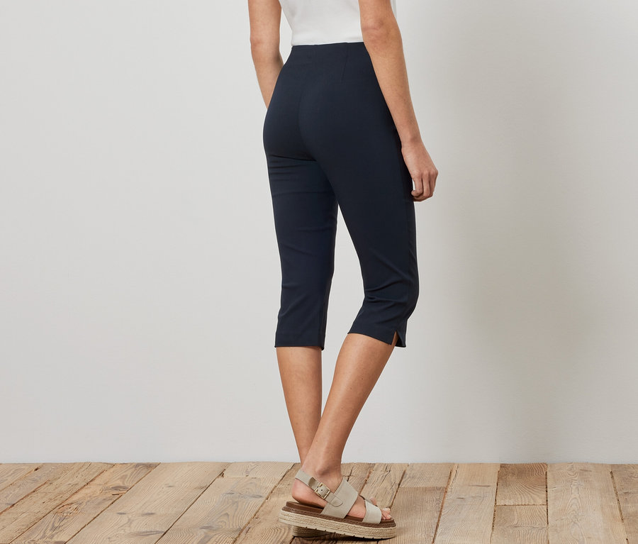 Une femme porte un pantalon 3/4 stretch bleu marine et des sandales.