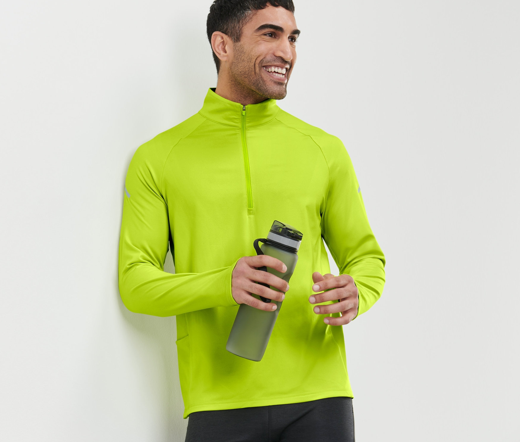 Un homme souriant tient une bouteille d'eau et porte un t-shirt technique thermique vert fluo.