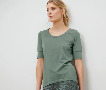 Une femme porte un t-shirt technique vert à demi-manches et un legging à imprimé feuille.