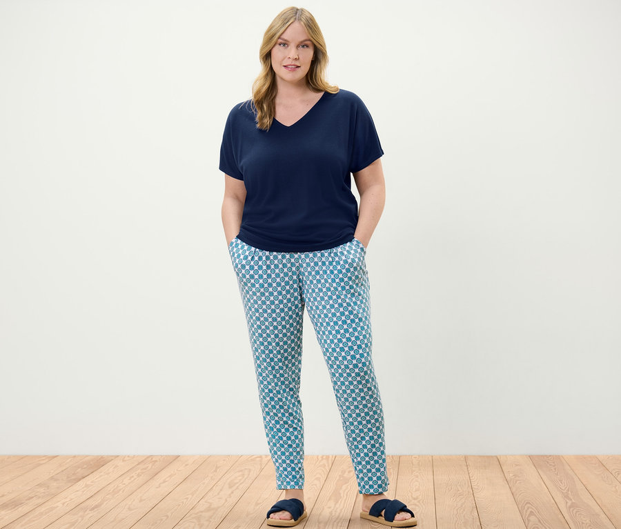 Une femme debout portant un pantalon en jersey avec motif intégral et une blouse structurée bleu foncé.