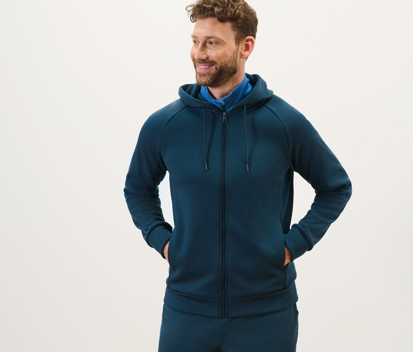 Homme barbu debout portant une veste technique à capuche.