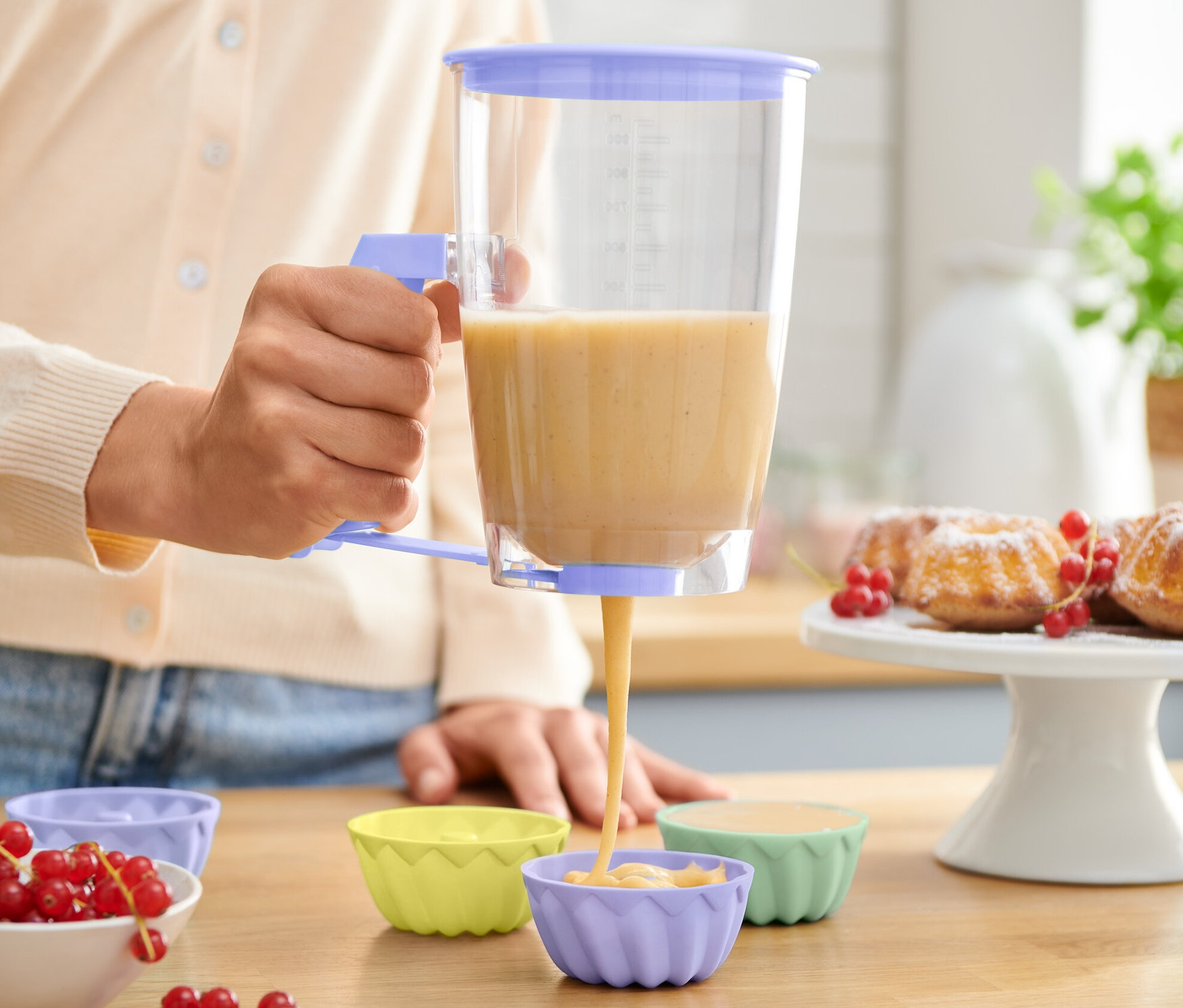 Une femme utilise un portionneur de pâte pour remplir des moules à muffins en silicone.