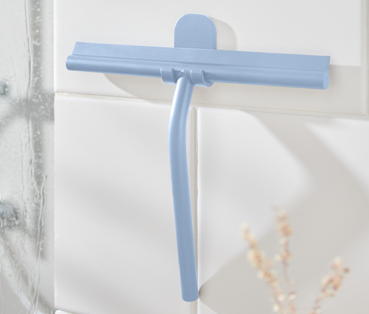 Raclette de salle de bain bleue avec support mural sur des carreaux blancs à côté de la douche.