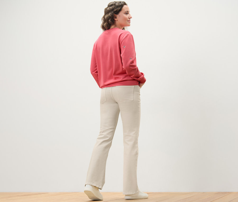 Une femme, vue de dos, porte un jean bootcut – Coupe « Lou », blanc crème et un sweat-shirt rose.