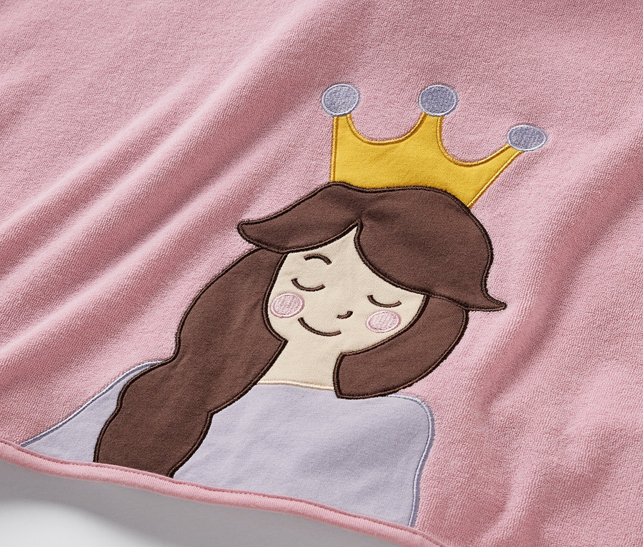 Gros plan sur un poncho rose en tissu éponge orné d'un motif de princesse avec des cheveux bruns et une couronne dorée.
