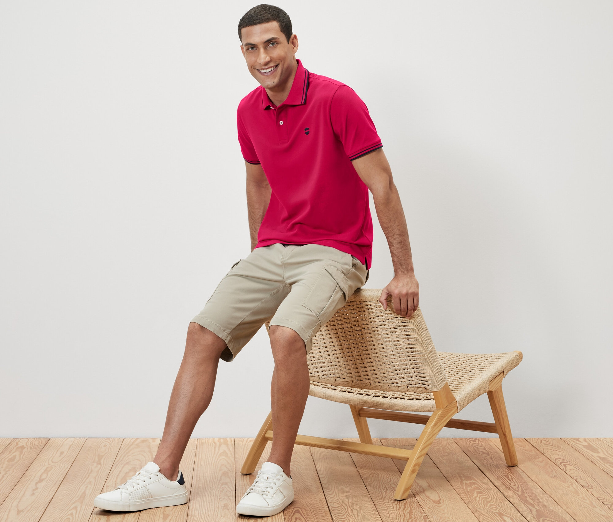 Un homme est assis sur une chaise en osier et porte un polo rose.