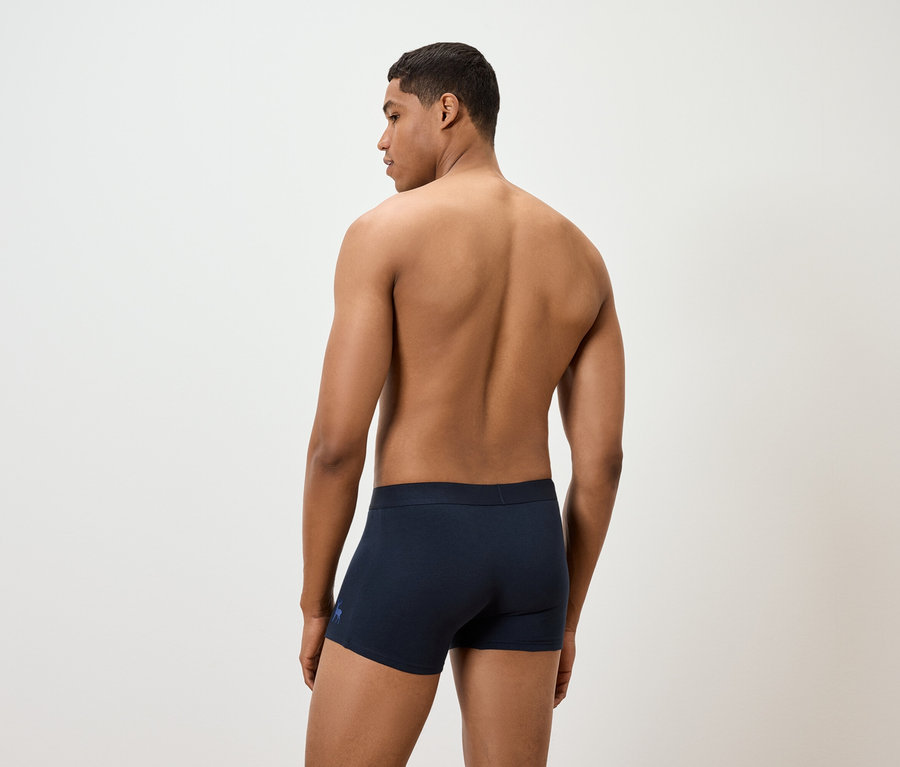 Un homme torse nu porte un caleçon boxeur bleu marine.