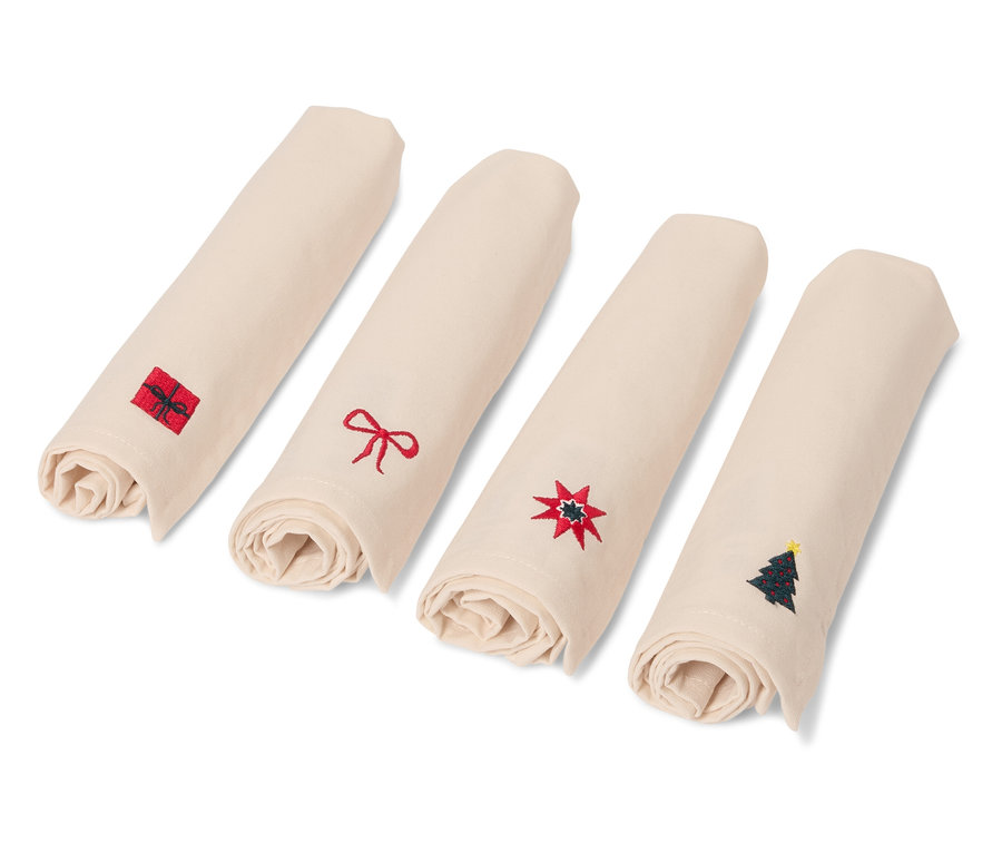 Quatre serviettes beiges roulées avec des motifs de Noël.
