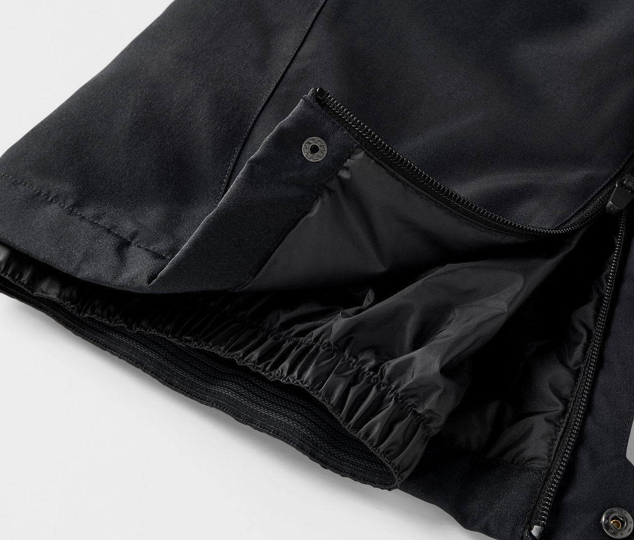 Détail d'un pantalon noir avec fermeture éclair ouverte et bouton-pression.
