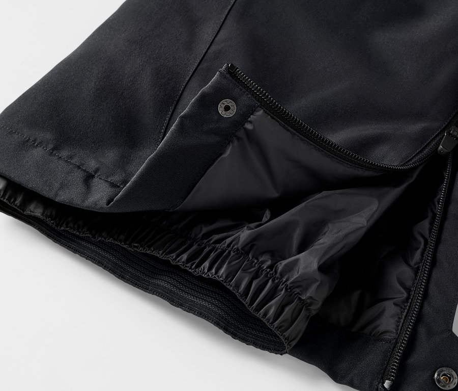 Détail d'un pantalon noir avec fermeture éclair ouverte et bouton-pression.