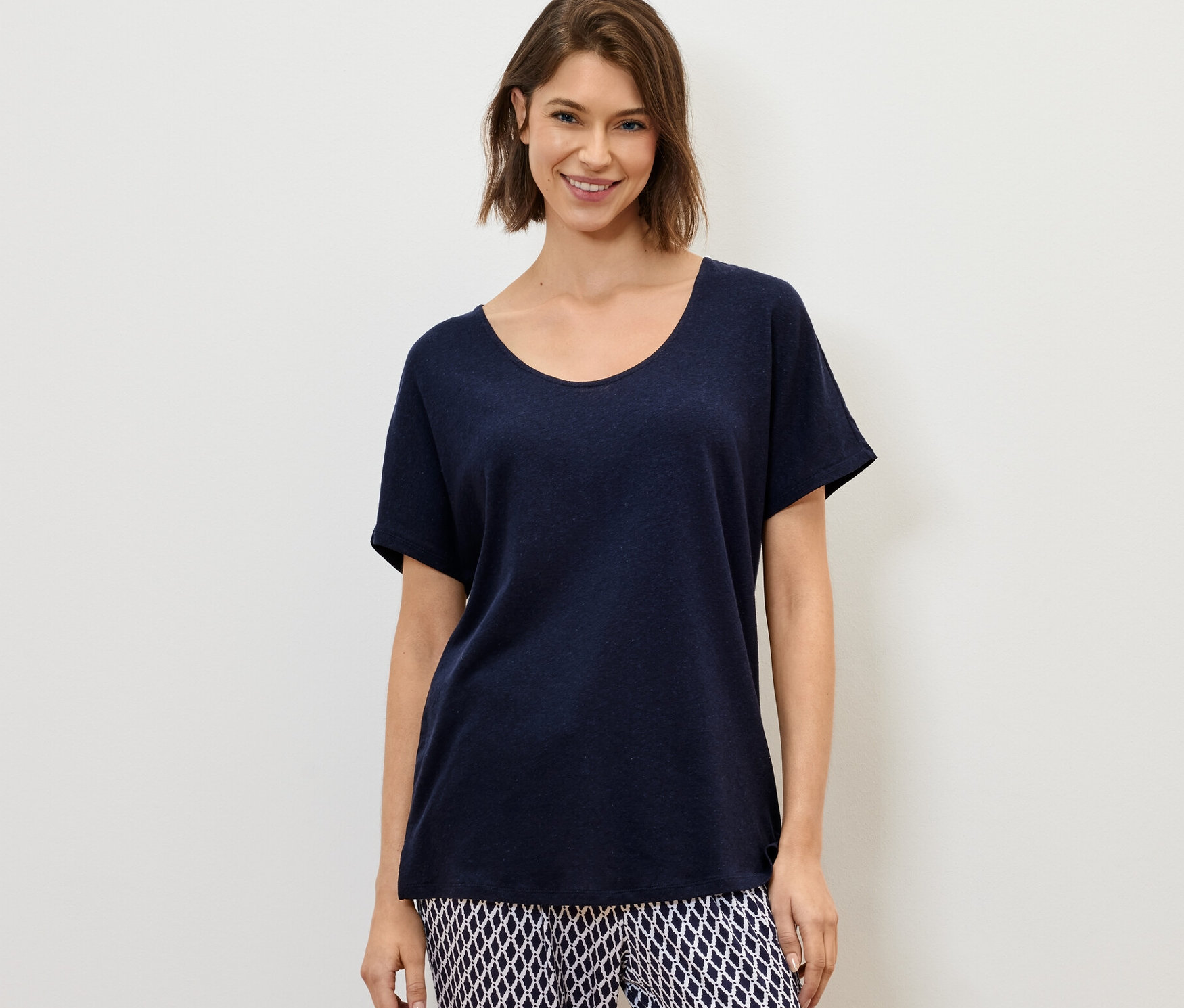 Une femme porte un t-shirt bleu marine en lin mélangé et un pantalon à motifs.