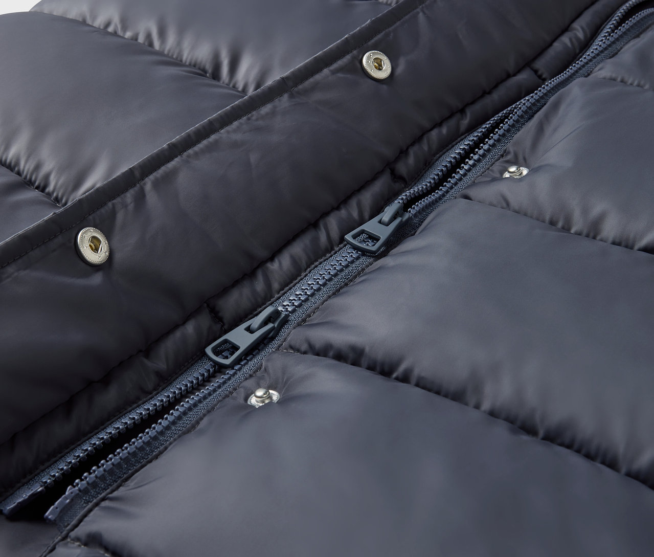 Gros plan d'une veste matelassée bleu marine avec boutons-pression argentés et fermeture éclair.
