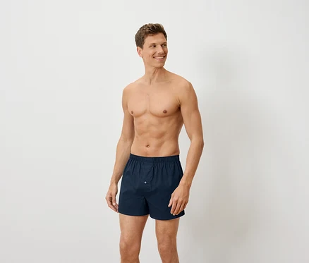 Un homme torse nu pose en boxer bleu marine.