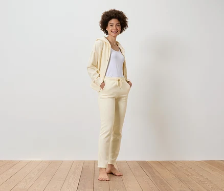 Une femme souriante avec une coupe afro se tient debout et porte un survêtement jaune avec un t-shirt blanc.