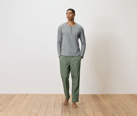 Un homme debout, les mains dans les poches d'un pantalon vert et d'une chemise grise à manches longues.