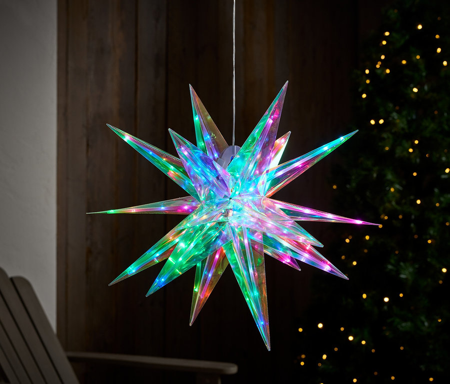 Étoile suspendue et illuminée en couleur avec des pointes devant un arbre avec des lumières.