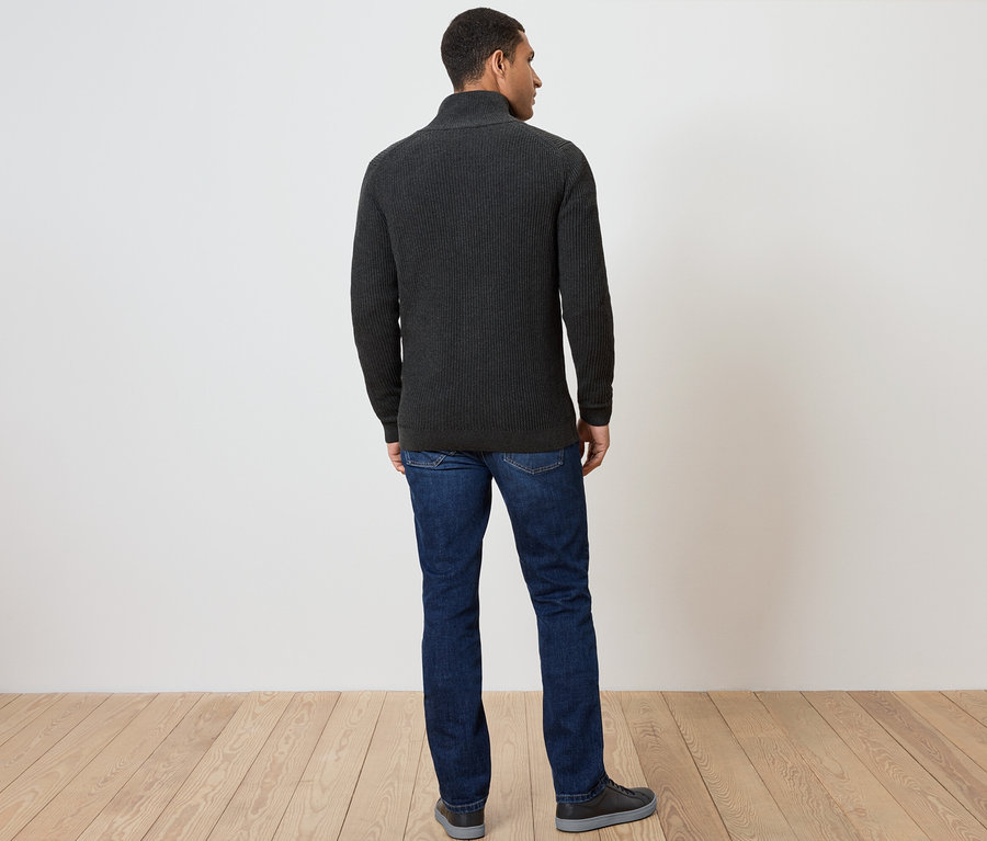 Un homme vu de dos porte un pull zippé gris foncé, un jean et des chaussures.