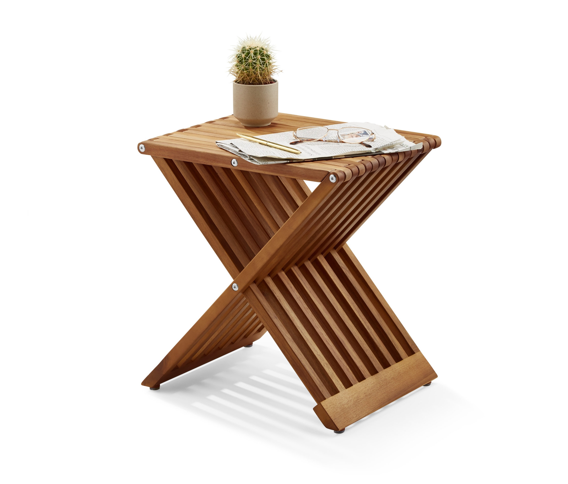 Sur un tabouret pliant reposent un cactus en pot, des lunettes, un stylo et un morceau de papier.