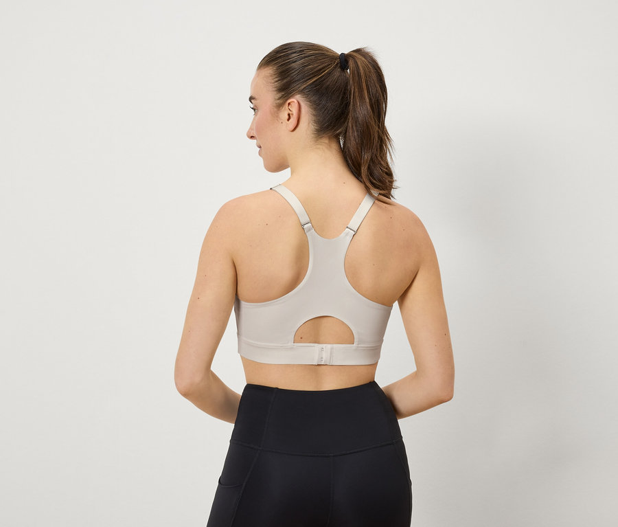 Femme de dos, portant un soutien-gorge de sport beige et un legging noir.