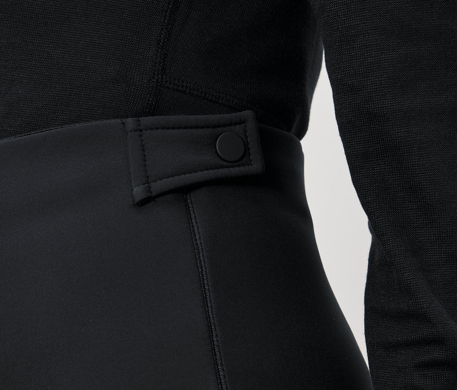 Détail d'un pantalon noir pour femme avec un bouton à la taille et un pull noir.